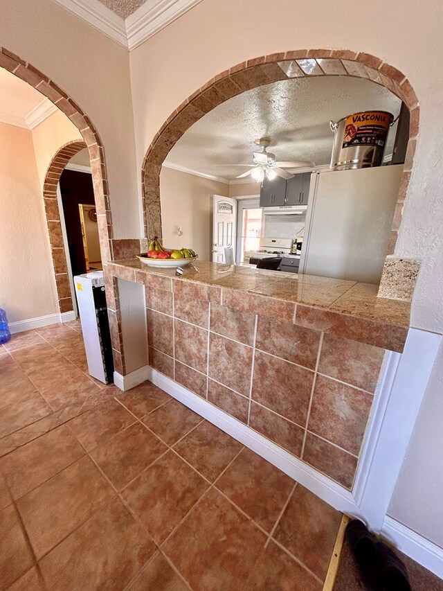 kitchen featuring tile patterned floors, ornamental molding, a textured ceiling, ceiling fan, and white gas stove