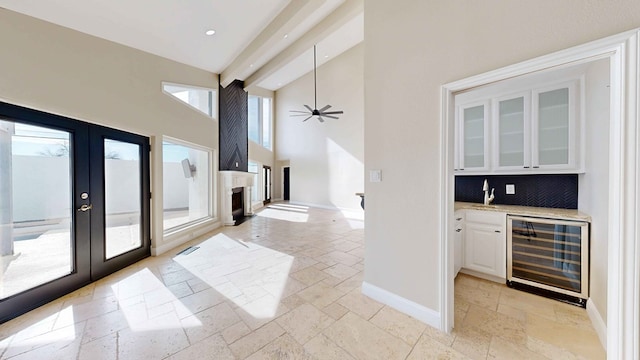 kitchen with high vaulted ceiling, light stone counters, white cabinets, french doors, and beverage cooler