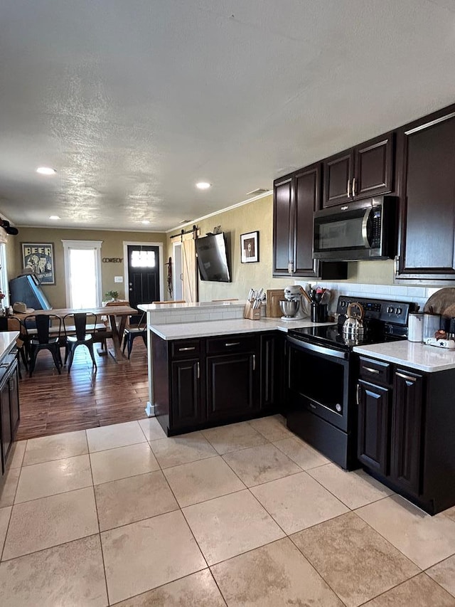 kitchen featuring black / electric stove, light tile patterned floors, a peninsula, light countertops, and a barn door