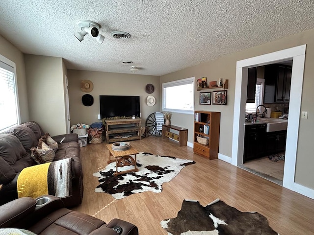 living room featuring baseboards, light wood-style floors, visible vents, and a textured ceiling