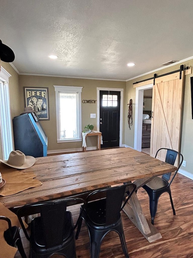 dining area featuring wood finished floors, visible vents, ornamental molding, a textured ceiling, and a barn door