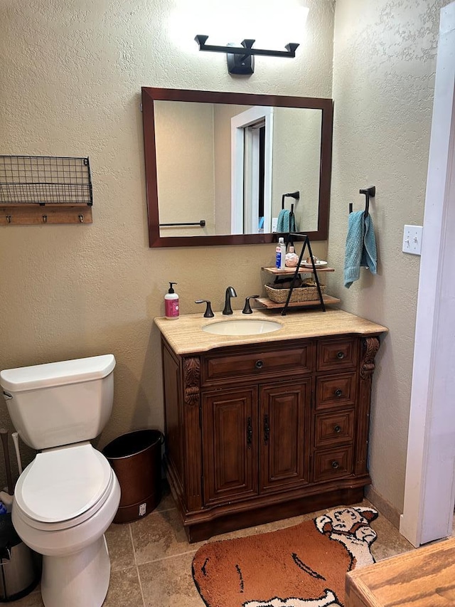 bathroom featuring baseboards, toilet, vanity, and a textured wall