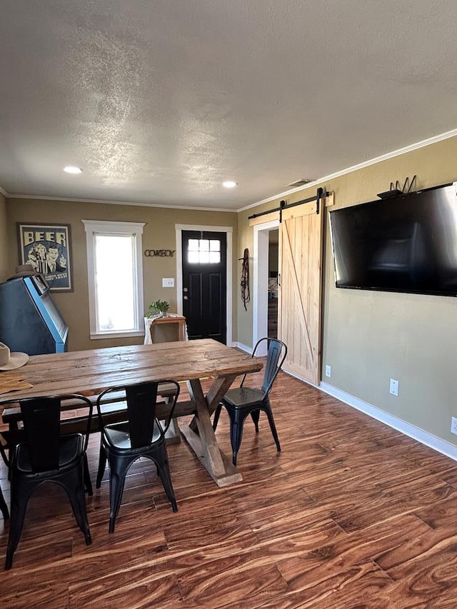 dining space featuring crown molding, baseboards, dark wood-type flooring, a barn door, and a textured ceiling