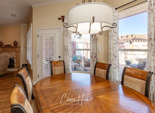 dining area featuring a fireplace with raised hearth, crown molding, and wood finished floors