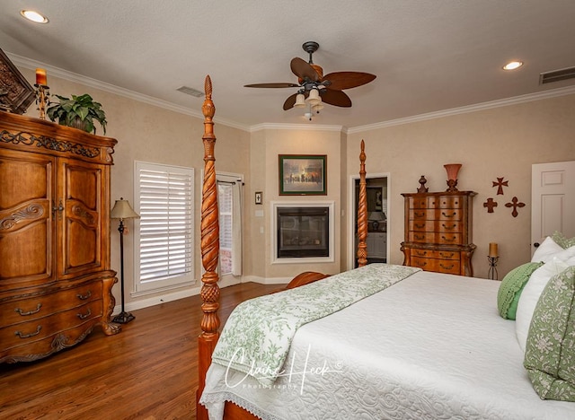 bedroom with a glass covered fireplace, wood finished floors, visible vents, and ornamental molding