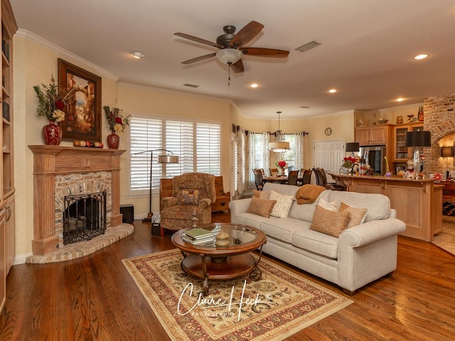 living room featuring a stone fireplace, ceiling fan, dark wood-type flooring, and ornamental molding