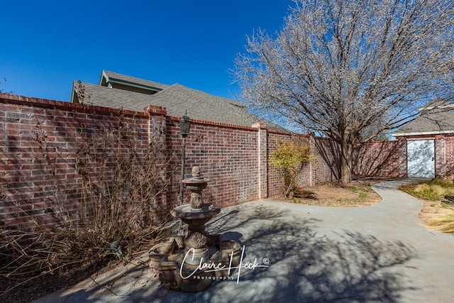 view of property exterior featuring a patio, brick siding, roof with shingles, and fence