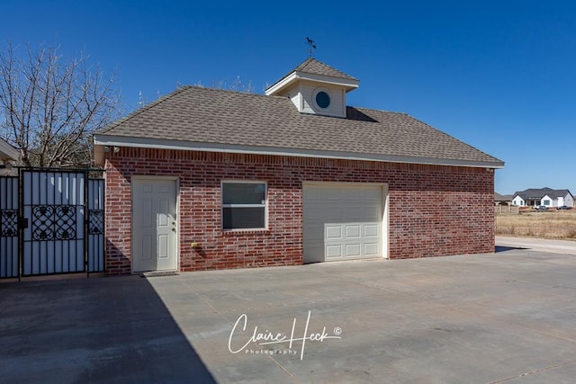 exterior space with brick siding, roof with shingles, an attached garage, and a gate