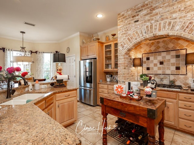 kitchen with stainless steel fridge, pendant lighting, light brown cabinetry, and sink