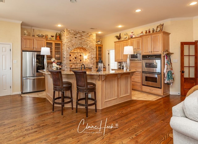 kitchen with glass insert cabinets, light stone countertops, light wood-type flooring, ornamental molding, and stainless steel appliances