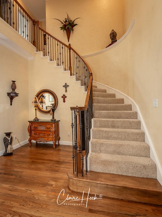 stairs featuring wood finished floors, baseboards, and a towering ceiling