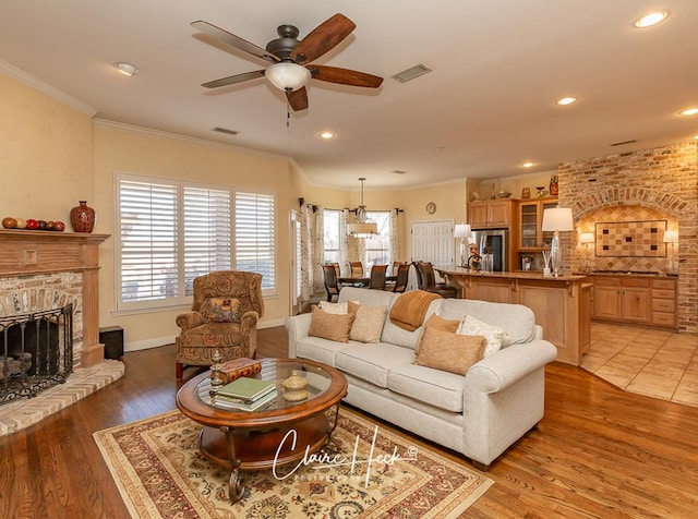 living area featuring crown molding, a fireplace, visible vents, and light wood-type flooring