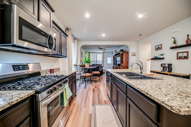 kitchen featuring ceiling fan, sink, stainless steel appliances, light stone counters, and light wood-type flooring