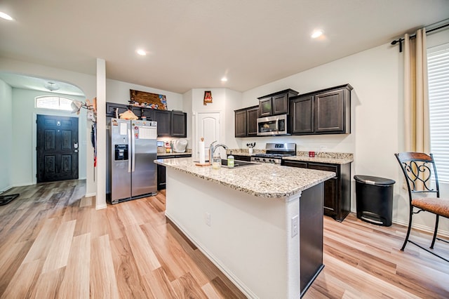 kitchen featuring sink, light stone counters, an island with sink, appliances with stainless steel finishes, and light wood-type flooring