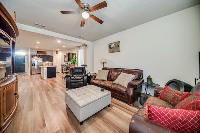 living room featuring ceiling fan, a textured ceiling, and light hardwood / wood-style flooring