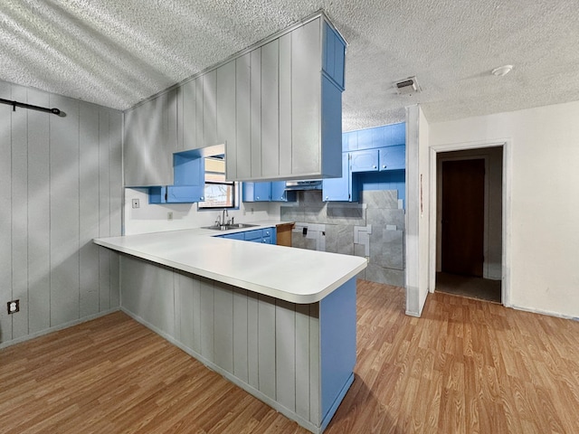 kitchen featuring sink, light hardwood / wood-style floors, kitchen peninsula, blue cabinetry, and a textured ceiling