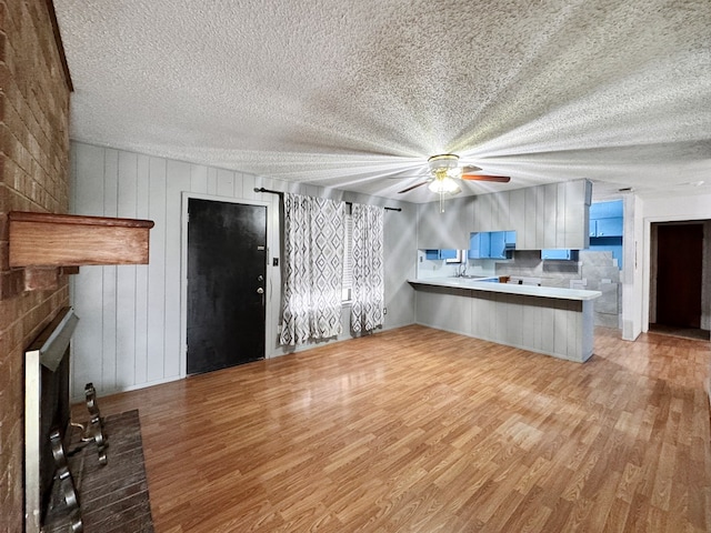 unfurnished living room featuring ceiling fan, a fireplace, light hardwood / wood-style flooring, and a textured ceiling