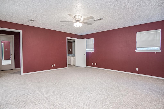 empty room with ceiling fan, light colored carpet, and a textured ceiling