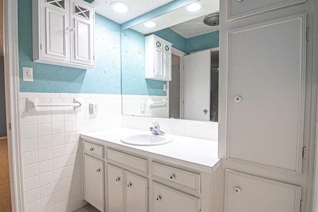 bathroom featuring a textured ceiling, vanity, and tile walls