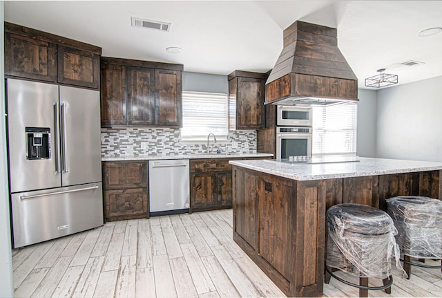 kitchen with a breakfast bar, stainless steel appliances, plenty of natural light, and premium range hood