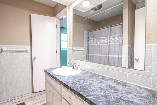 bathroom with wood-type flooring, vanity, a textured ceiling, and tile walls