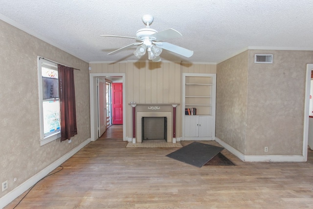 unfurnished living room with ornamental molding, built in shelves, a textured ceiling, ceiling fan, and light hardwood / wood-style floors