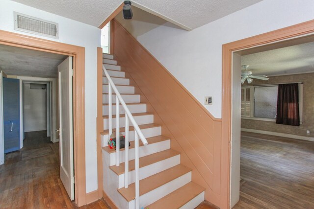 stairs with ceiling fan, wooden walls, wood-type flooring, and a textured ceiling