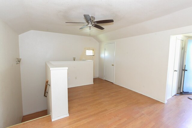 empty room with a textured ceiling, ceiling fan, vaulted ceiling, and light wood-type flooring