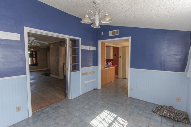 unfurnished dining area featuring light wood-type flooring, ceiling fan with notable chandelier, a textured ceiling, vaulted ceiling, and wood walls