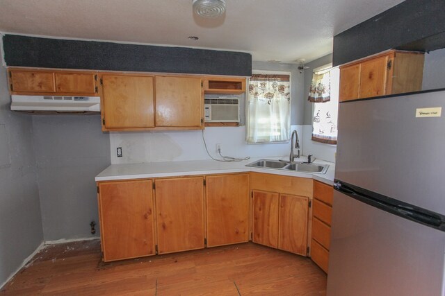 kitchen with light wood-type flooring, stainless steel refrigerator, an AC wall unit, and sink