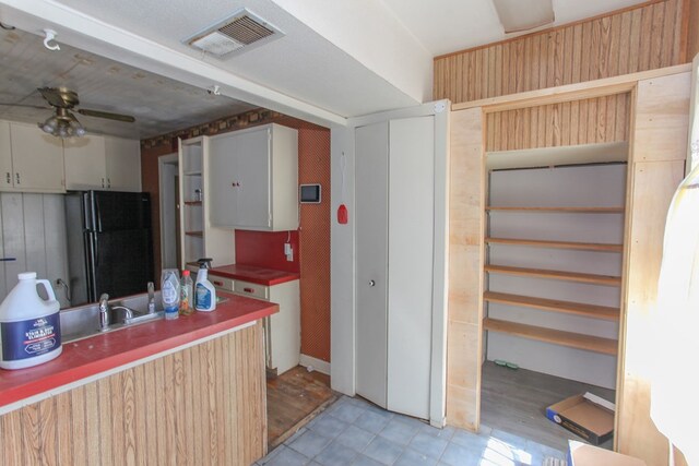 kitchen featuring ceiling fan, black refrigerator, light hardwood / wood-style floors, and wooden walls