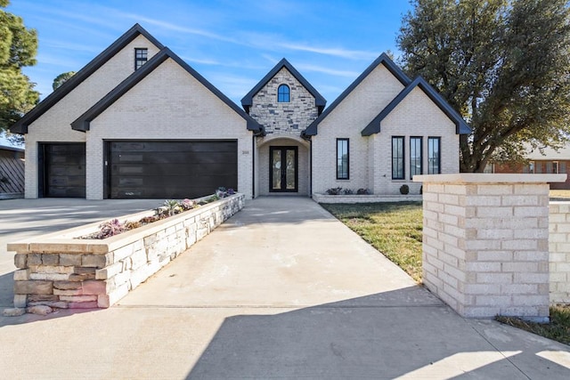 french country home with a garage, concrete driveway, and brick siding