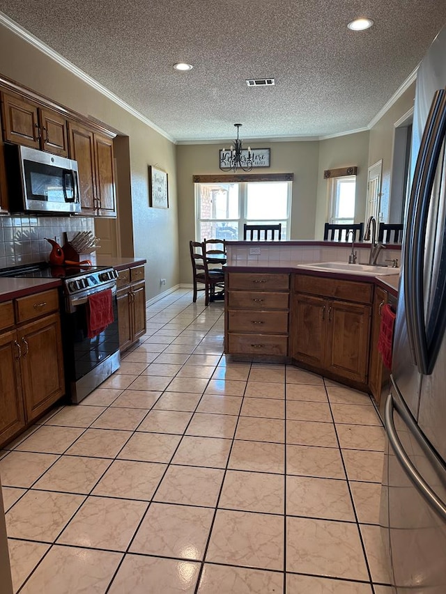 kitchen with light tile patterned floors, crown molding, appliances with stainless steel finishes, and a chandelier