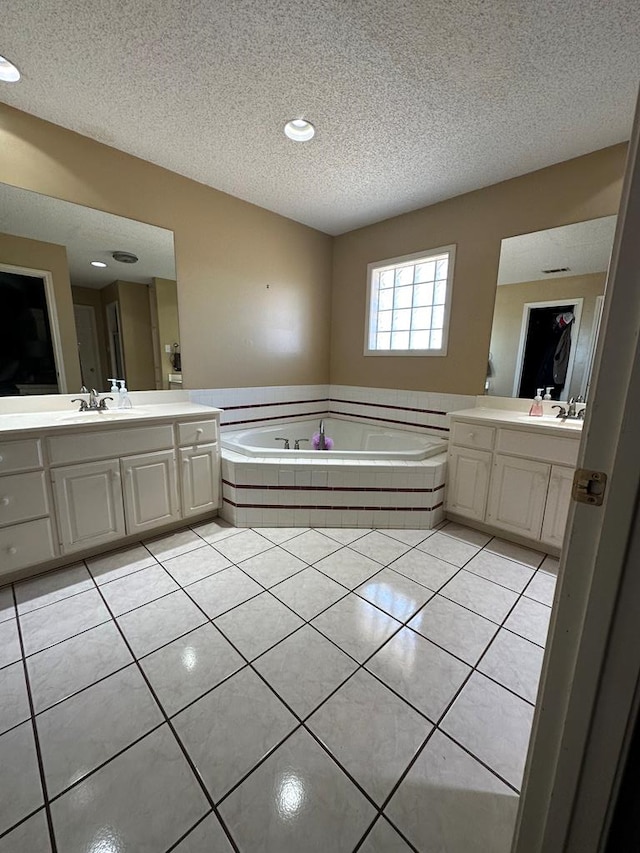 bathroom featuring vanity, a textured ceiling, tiled bath, and tile patterned floors