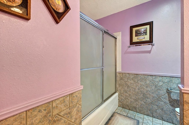 3013 Whittle Way, Midland, TX 79707 - bathroom with tile walls, wainscoting, bath / shower combo with glass door, a textured ceiling, and a textured wall