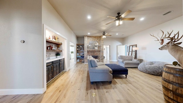 living room featuring built in shelves, a fireplace, wet bar, and light hardwood / wood-style floors