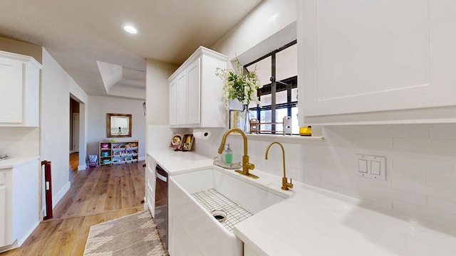 kitchen featuring sink, light hardwood / wood-style flooring, black dishwasher, decorative backsplash, and white cabinets