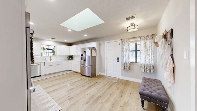 kitchen with a skylight, sink, white cabinets, stainless steel appliances, and light wood-type flooring