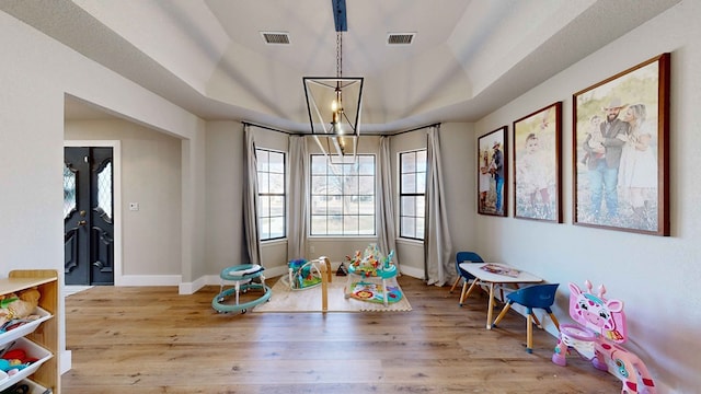 game room featuring an inviting chandelier, light hardwood / wood-style floors, and a raised ceiling