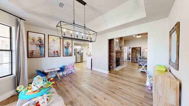 recreation room featuring a tray ceiling, a fireplace, and light wood-type flooring