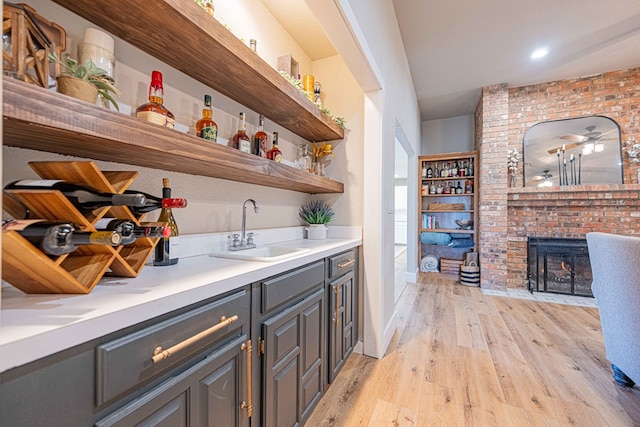 bar with light hardwood / wood-style flooring, sink, a fireplace, and gray cabinetry