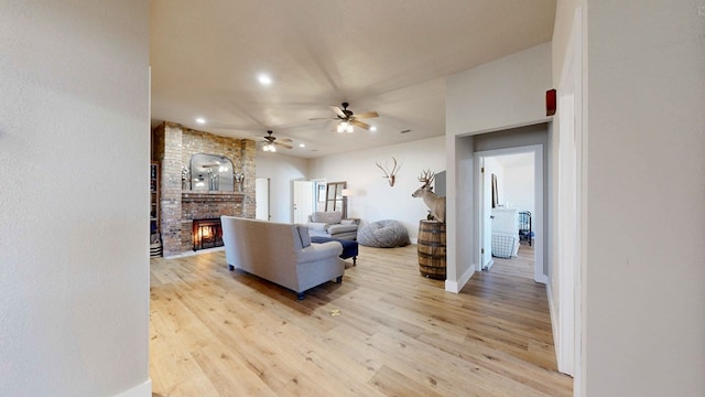 living room featuring ceiling fan, a fireplace, and light wood-type flooring