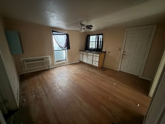 unfurnished living room featuring baseboards, a wall mounted air conditioner, ceiling fan, and wood-type flooring