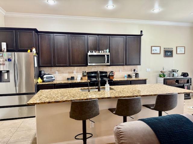 1406 Wrangler Ln, Midland, TX 79705 - kitchen featuring stainless steel appliances, a breakfast bar, light stone counters, tasteful backsplash, and crown molding