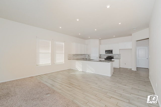 kitchen featuring open floor plan, a peninsula, white cabinetry, backsplash, and appliances with stainless steel finishes