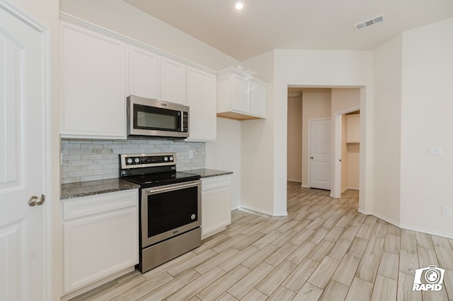 kitchen featuring light wood-style floors, white cabinets, dark stone countertops, appliances with stainless steel finishes, and decorative backsplash