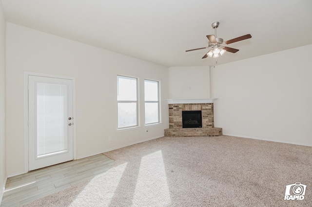 unfurnished living room featuring light carpet, a brick fireplace, baseboards, and a ceiling fan