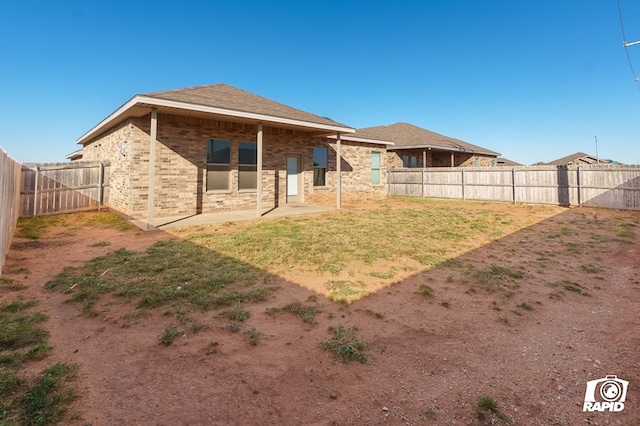 rear view of house featuring brick siding, a fenced backyard, a patio, and a lawn