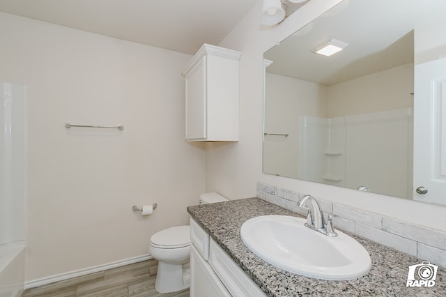 bathroom with vanity, toilet, a shower, wood finished floors, and baseboards