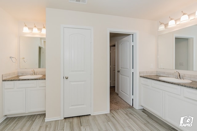 bathroom with two vanities, visible vents, a sink, and wood tiled floor